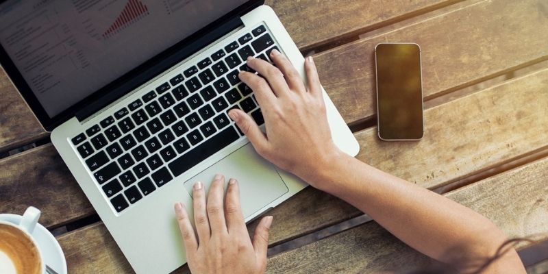 Closeup of a person on their laptop with coffee and their phone